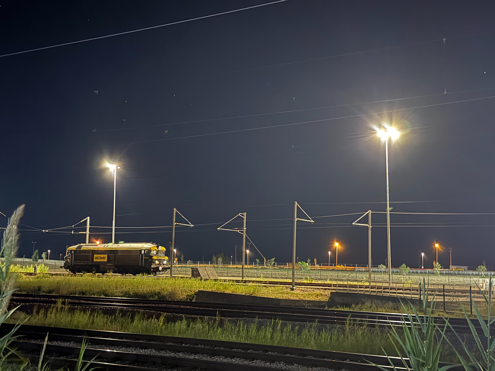 A MEDWAY locomotive standing among railway tracks under lights at night