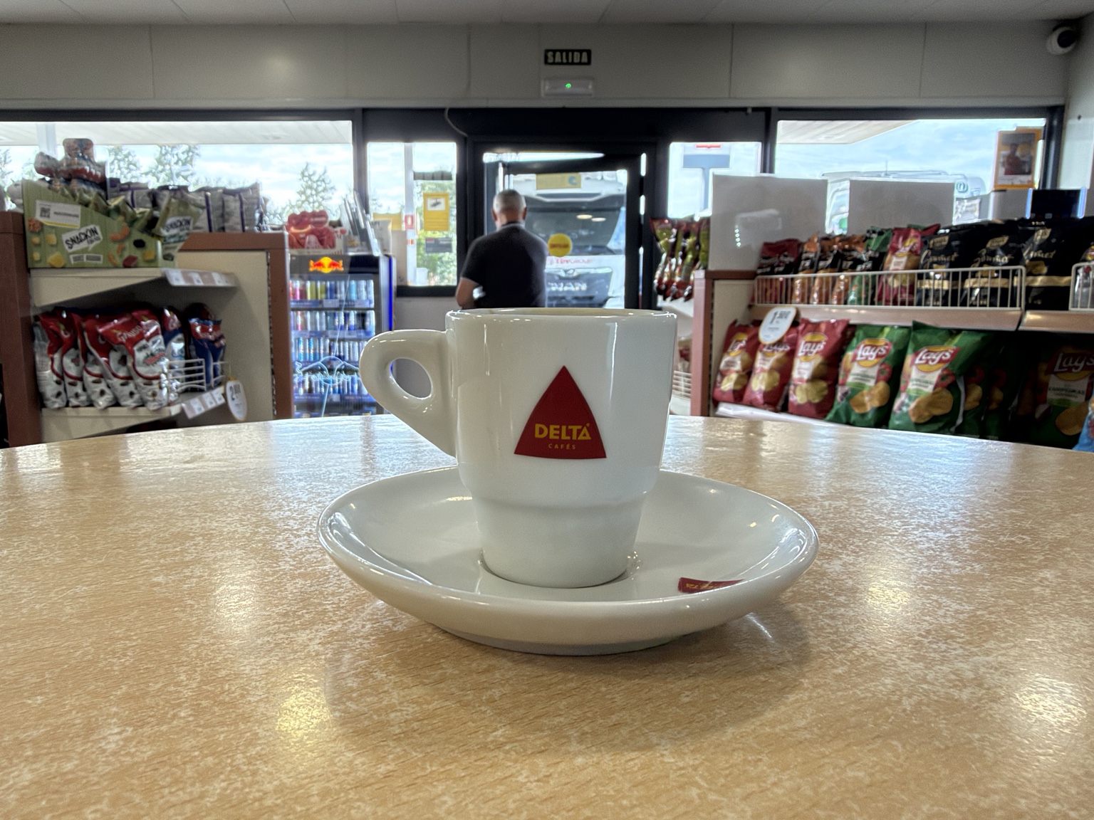 加油站商店里,桌上的白色Delta咖啡杯,后方是零食货架、门口的人与卡车