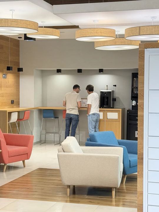 Dois vizinhos conversam junto à máquina de café sobre os doces e snacks dentro da caixa XIAOXIONG