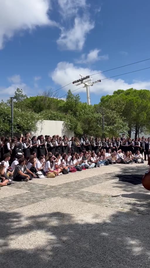 Uma tuna de estudantes com capas negras toca à sombra das árvores no Parque das Nações, rodeada de jovens de pé e sentados no chão